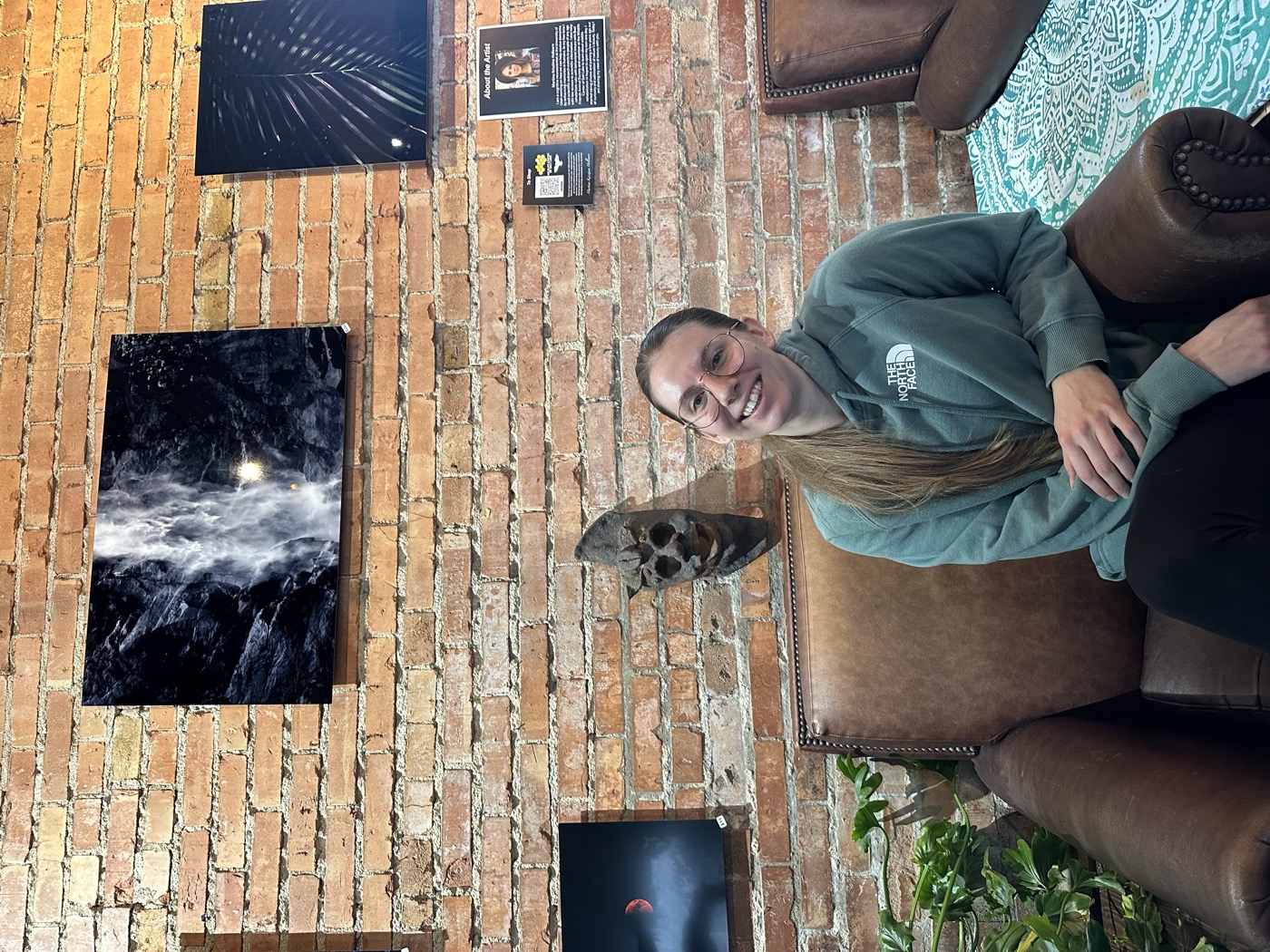 Martina Hollearn at her art show, seated below her framed prints